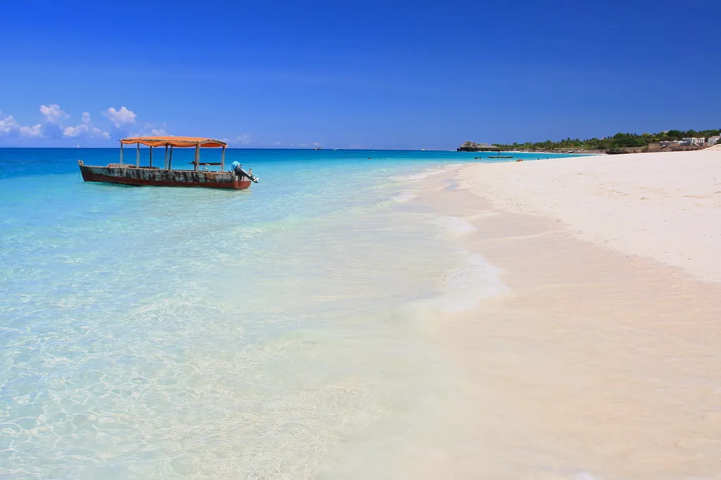Wooden boat with a canopy floating in clear shallow turquoise water off a white beach