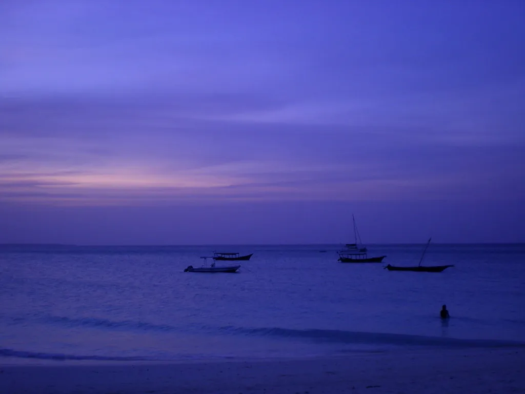 Purple and pink dusk sky over calm sea with silhouetted moored boats