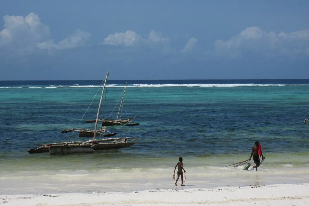 Traditional outrigger boats with masts in a turquoise lagoon, waves breaking on the reef behind