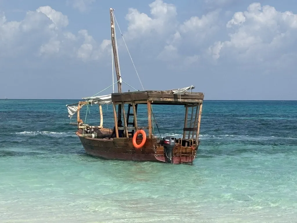 A traditional wooden dhow with a sun canopy and a life ring, anchored in clear turquoise water.