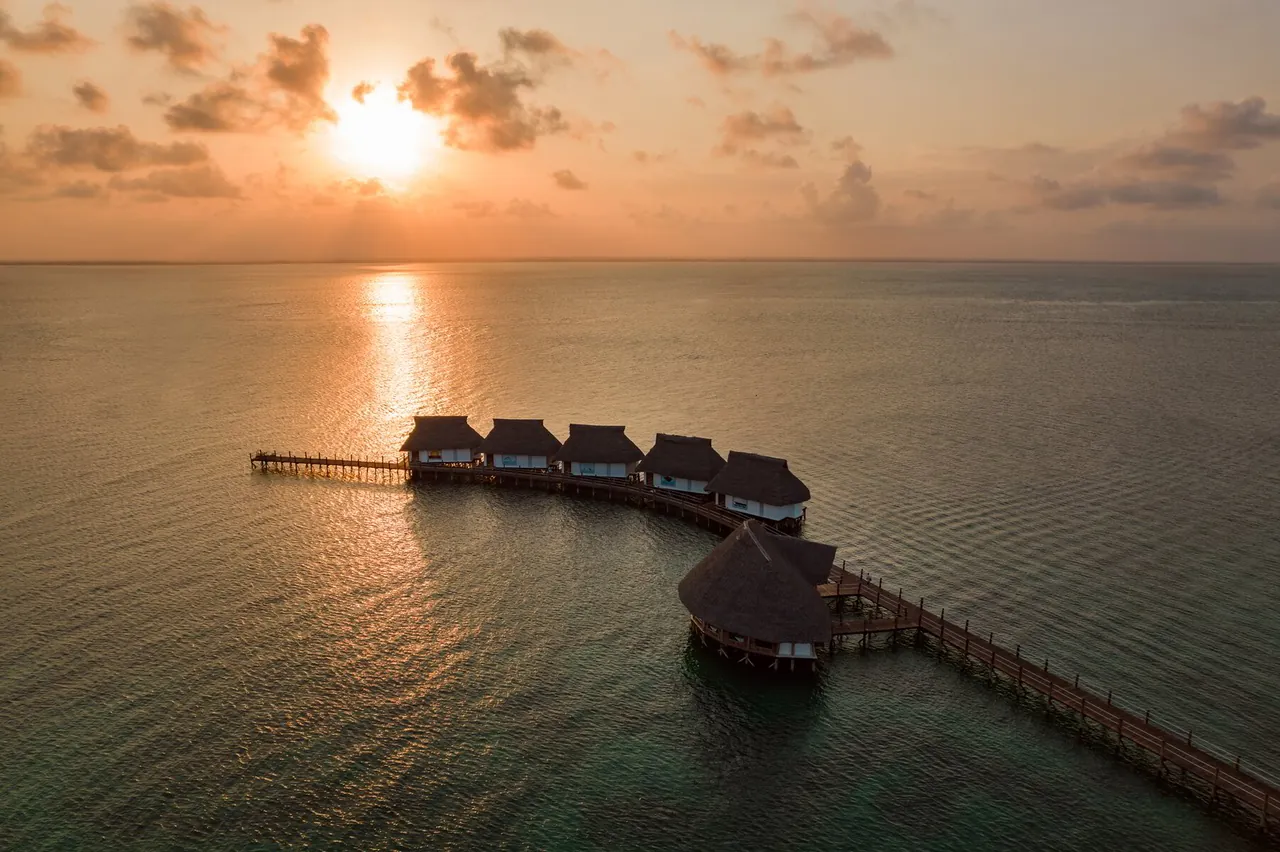 The sun setting over Chwaka Bay, with a resort's over-water villas on a jetty in silhouette