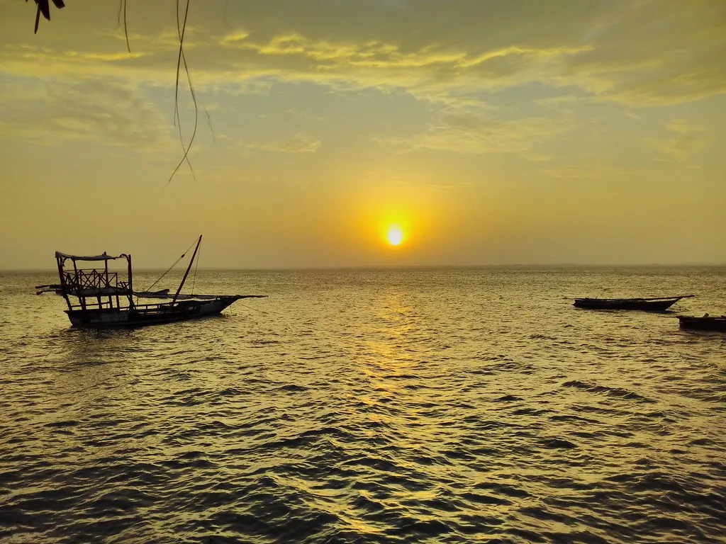 Sun setting over calm sea with a moored wooden boat silhouetted in the foreground