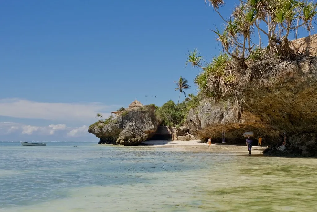 A small cove of shallow, clear water and white sand between overhanging rock outcrops topped with palms and pandanus.