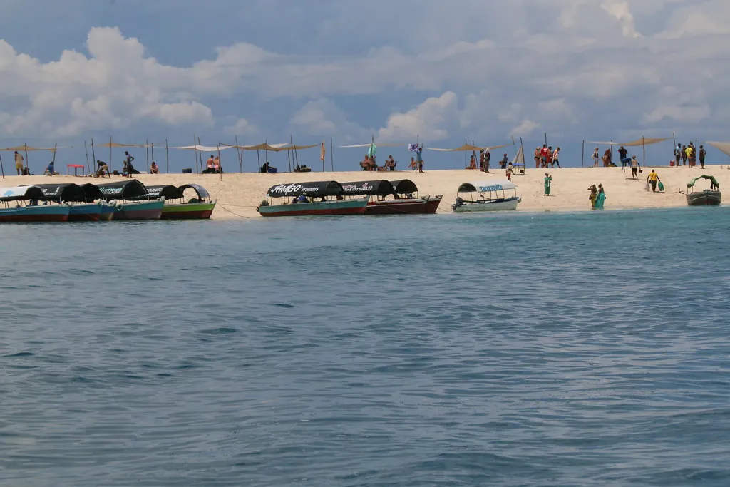 Closer view of the sandbank with tour boats pulled up and visitors walking on the sand under shade canopies