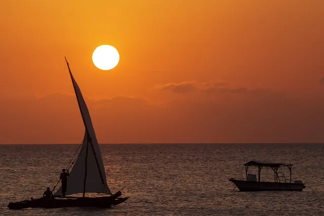 A sailing dhow against an orange sunset off Nungwi