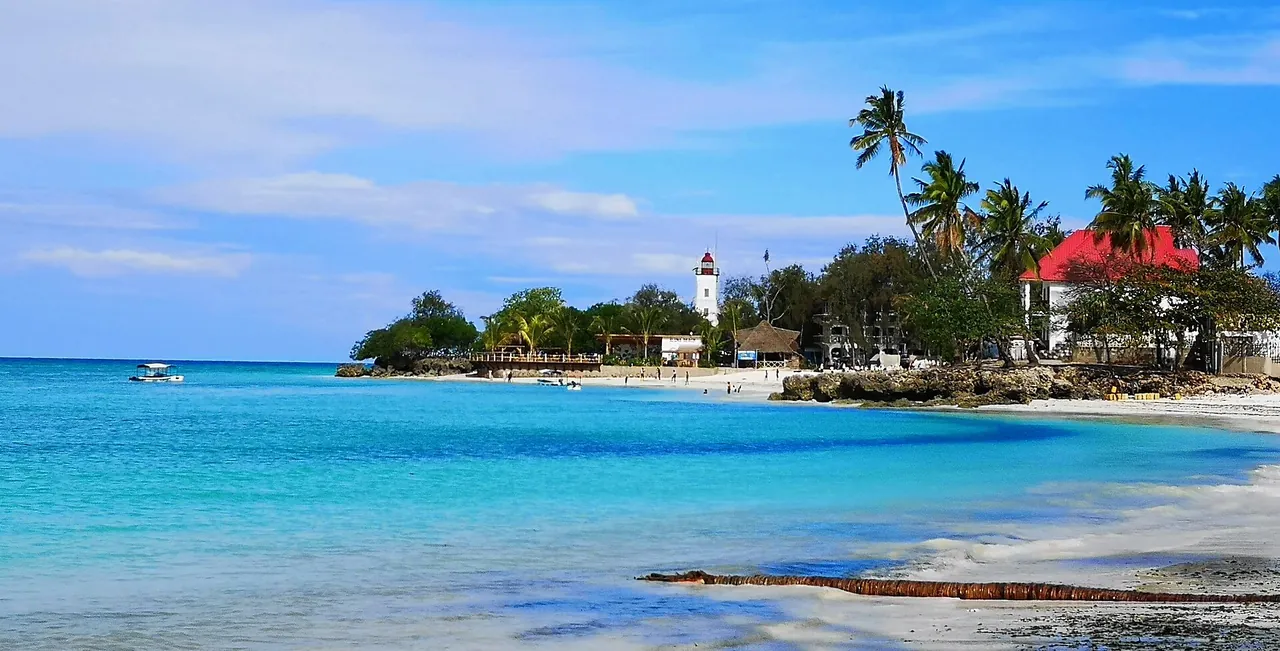 White lighthouse tower among palms behind a turquoise bay with a sandy shore