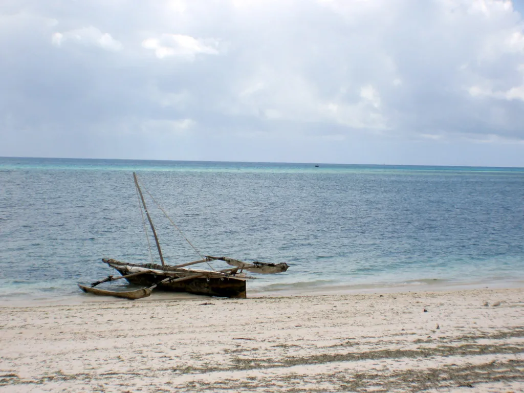 Traditional wooden outrigger fishing boat pulled up on white sand with the sea behind