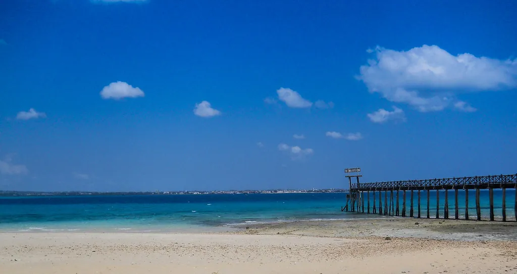 White sand beach and turquoise water with a long jetty under a blue sky