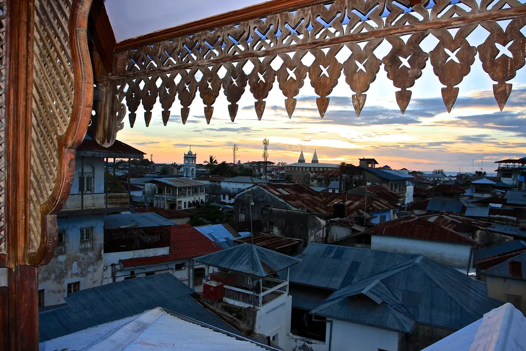 Stone Town's tin roofs and towers seen through the carved wooden fretwork of a rooftop pavilion