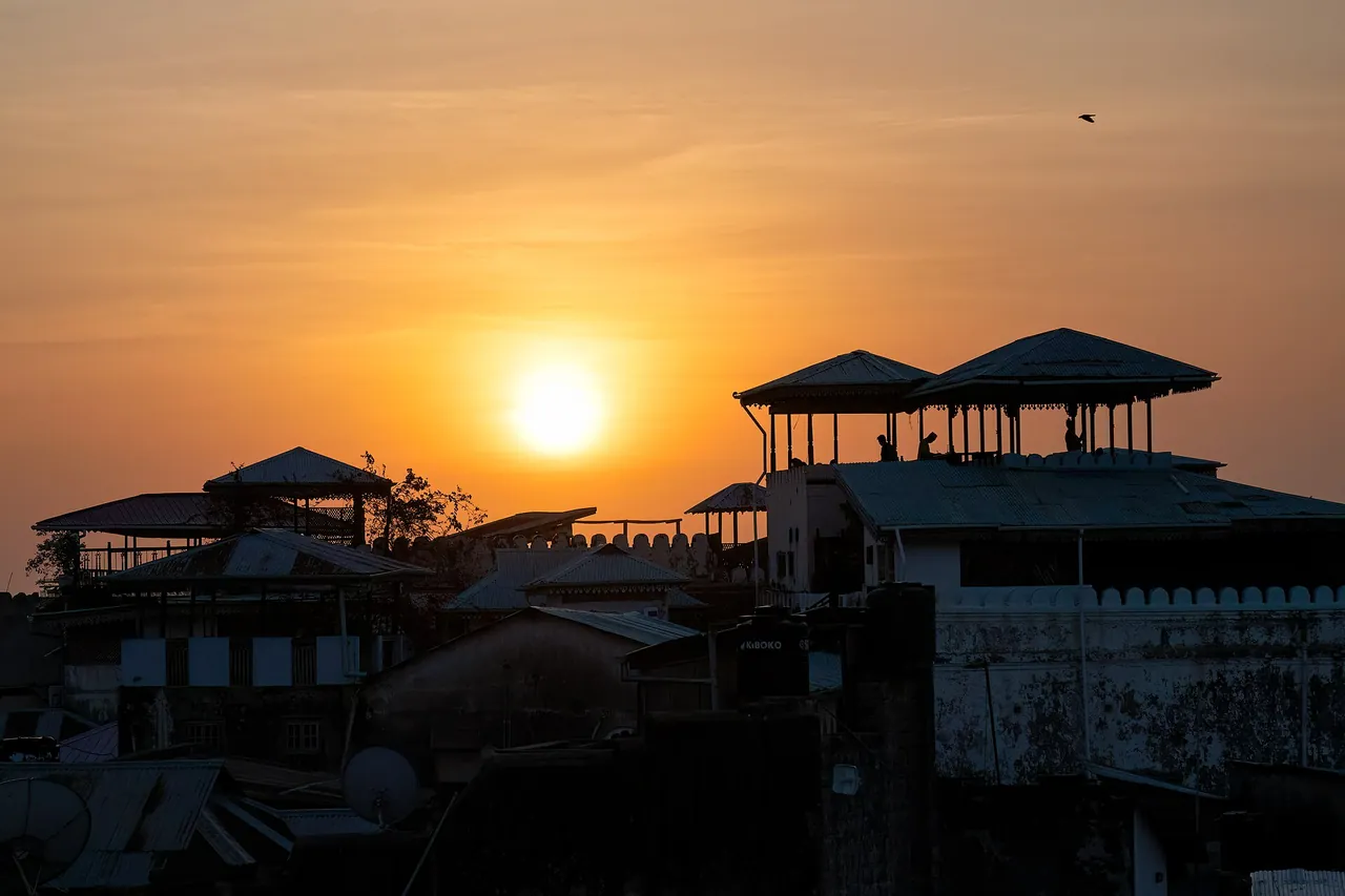Silhouetted Stone Town rooftop pavilions with the sun setting behind them in an orange sky