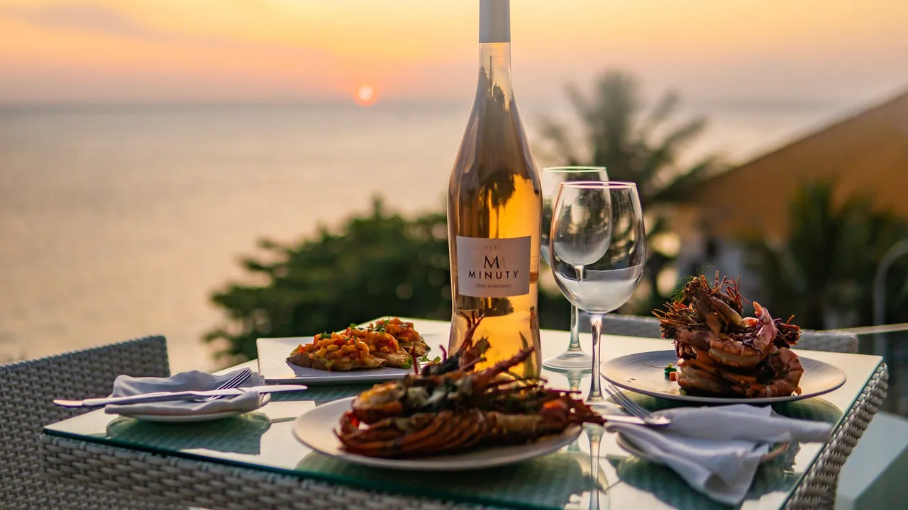 Seafood plates and a bottle of rosé on a terrace table at sunset over the sea