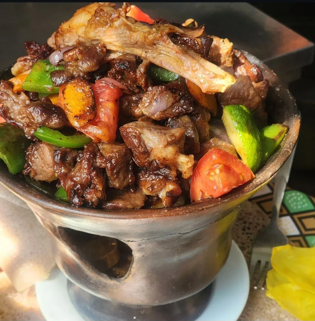 Sizzling lamb tibs with peppers and tomato served in a clay burner