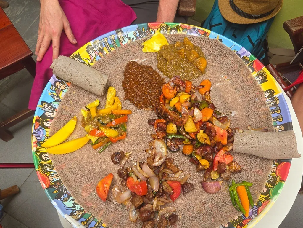 A large shared platter of injera with stews and vegetables on a colourful basket table