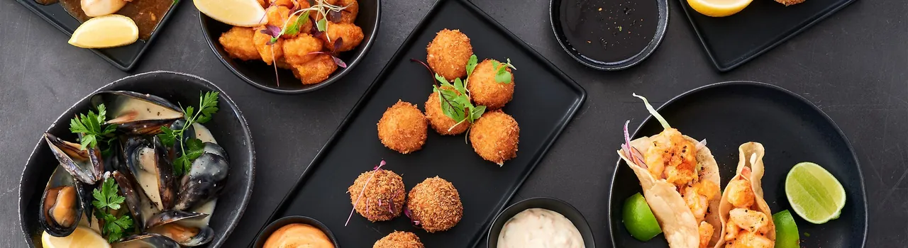 Overhead view of small plates of fried seafood bites, mussels and prawns on a dark table