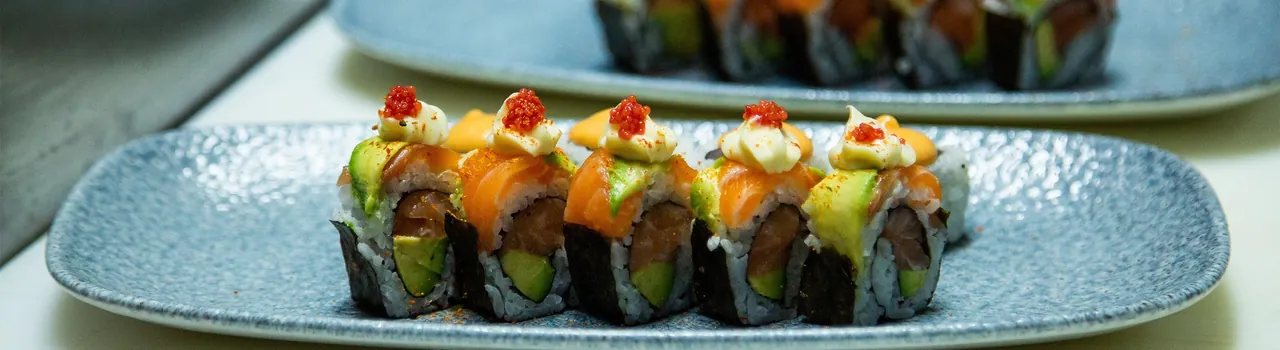 A row of salmon-topped sushi rolls on a pale blue plate
