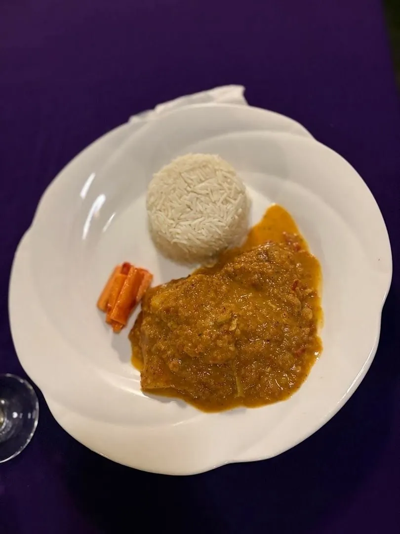 A curry in an orange sauce with a mound of rice and a few carrot sticks on a white plate.