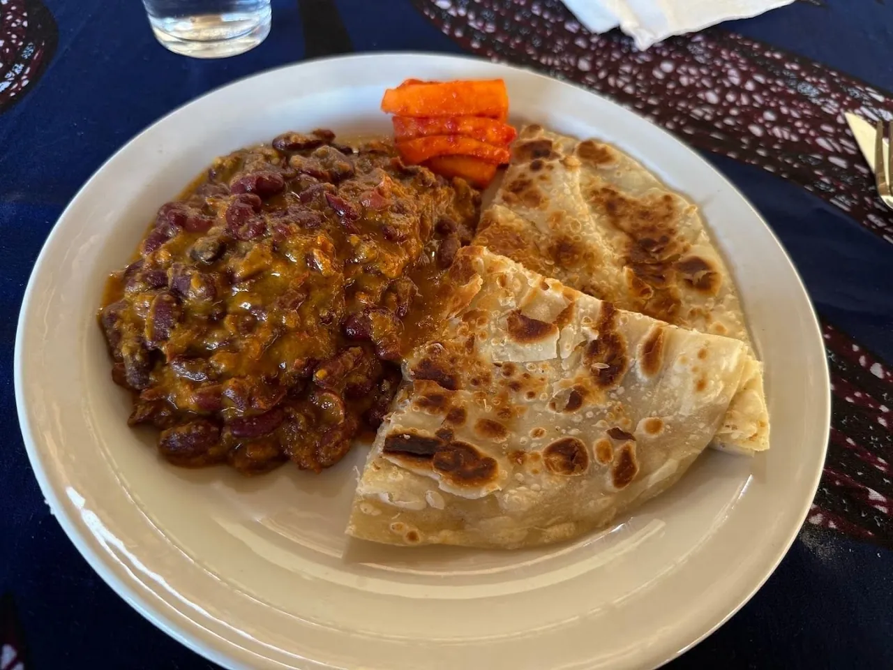 A bean stew alongside folded chapati flatbread on a white plate.