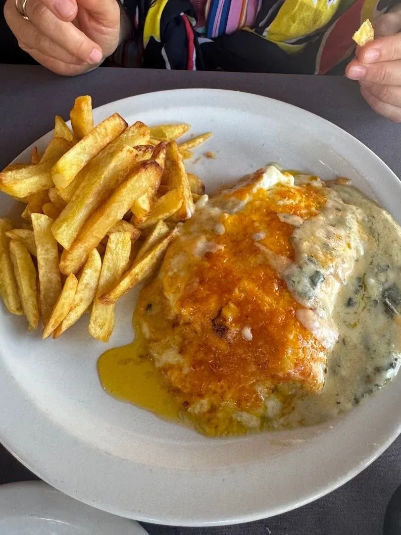 Chips next to a piece of fish in a creamy sauce on a white plate.