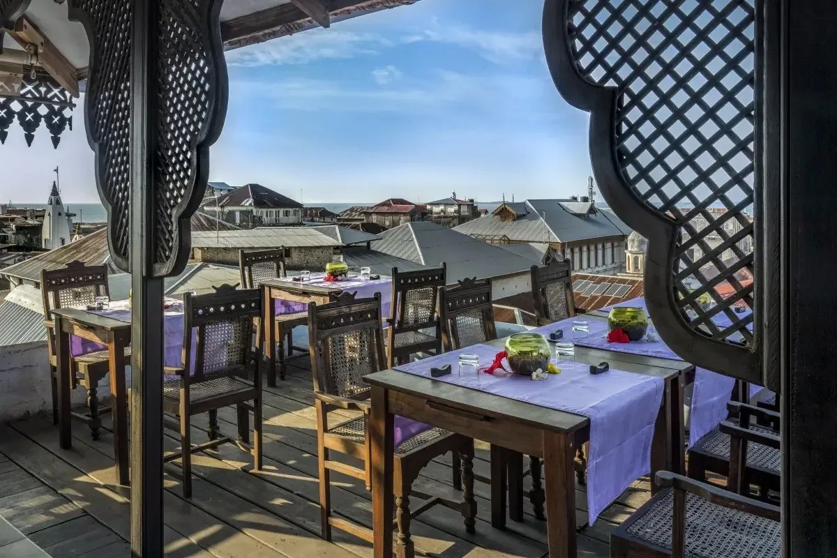 Set tables under the Tea House's carved wooden arches with tin roofs of Stone Town and the sea beyond