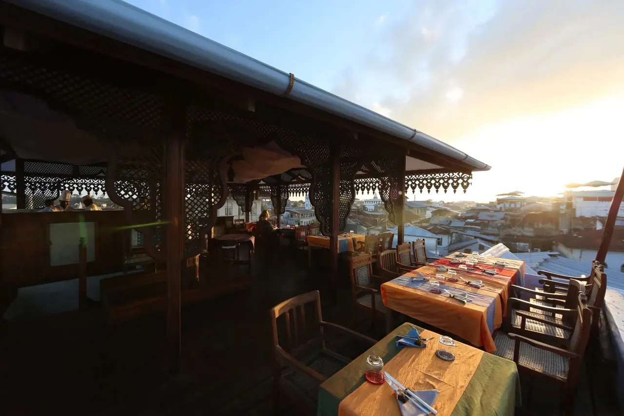 Tables laid with colourful cloths along the covered rooftop terrace in late-afternoon light