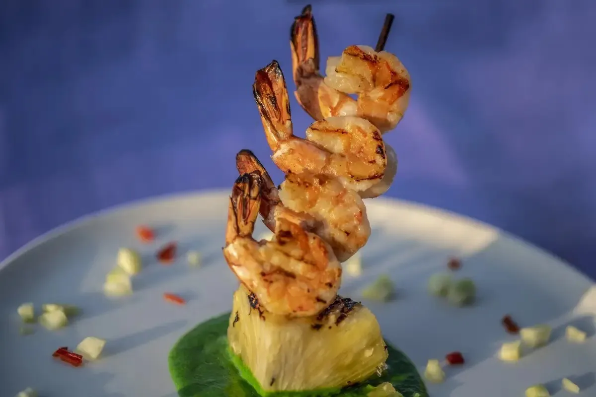 Grilled prawns on a skewer over pineapple on a white plate