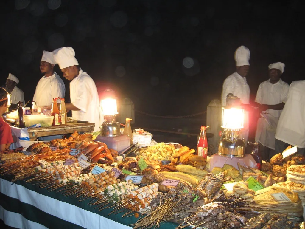 Cooks in white hats behind lantern-lit tables of seafood and skewers at night