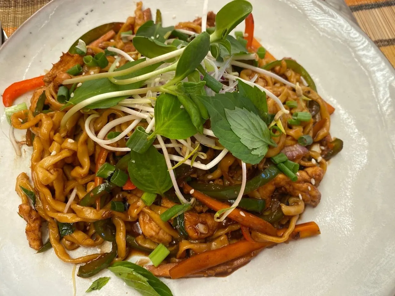 A plate of stir-fried noodles with vegetables, meat and fresh herbs