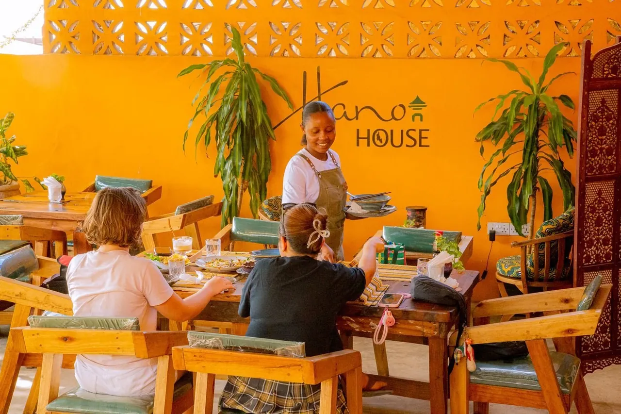 Diners at wooden tables in a bright orange room with plants and a Hanoi House sign on the wall