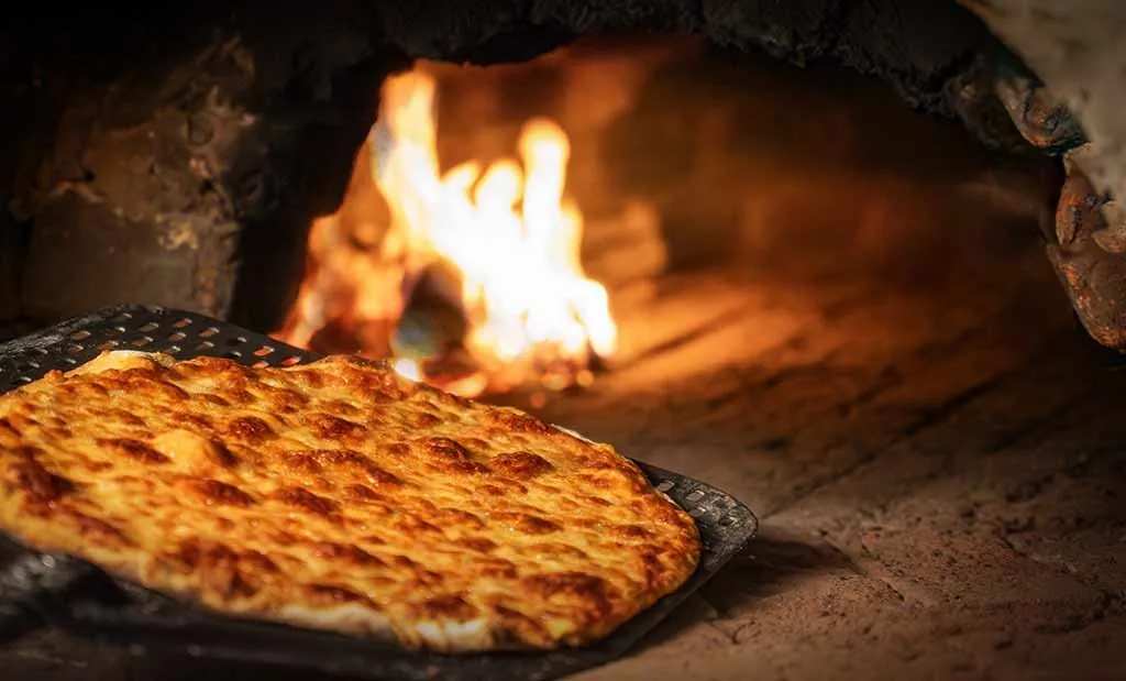 A thin, crisp pizza base on a peel in front of a wood fire