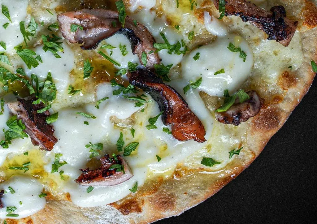 Close-up of a white pizza topped with octopus, cheese and parsley