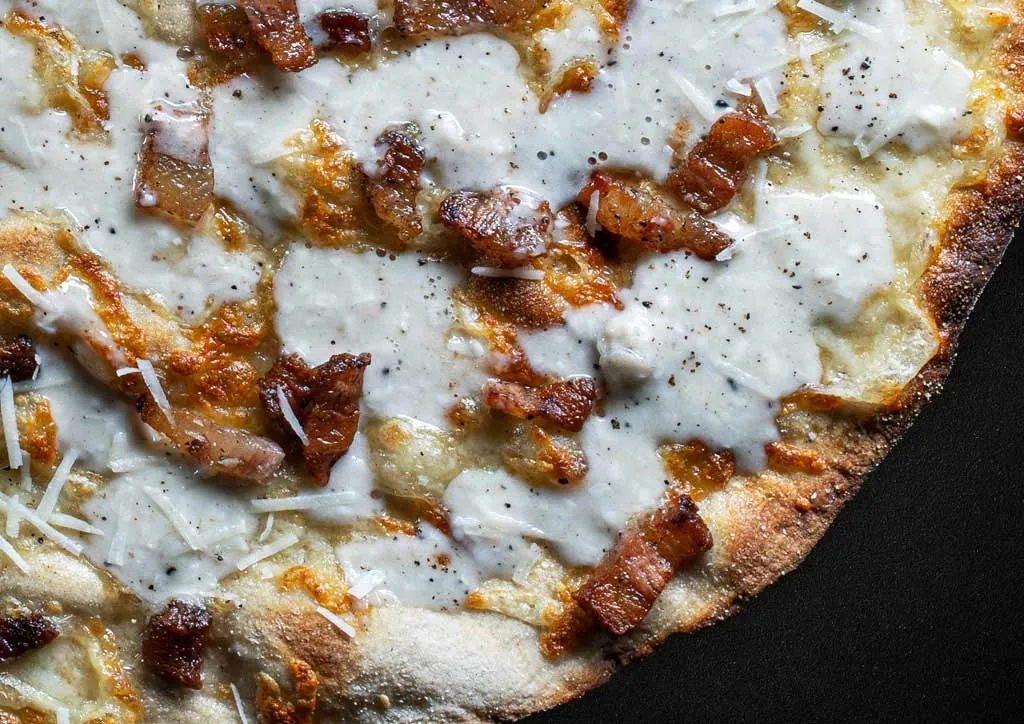 Close-up of a white pizza with pecorino, black pepper and crisp pork cheek