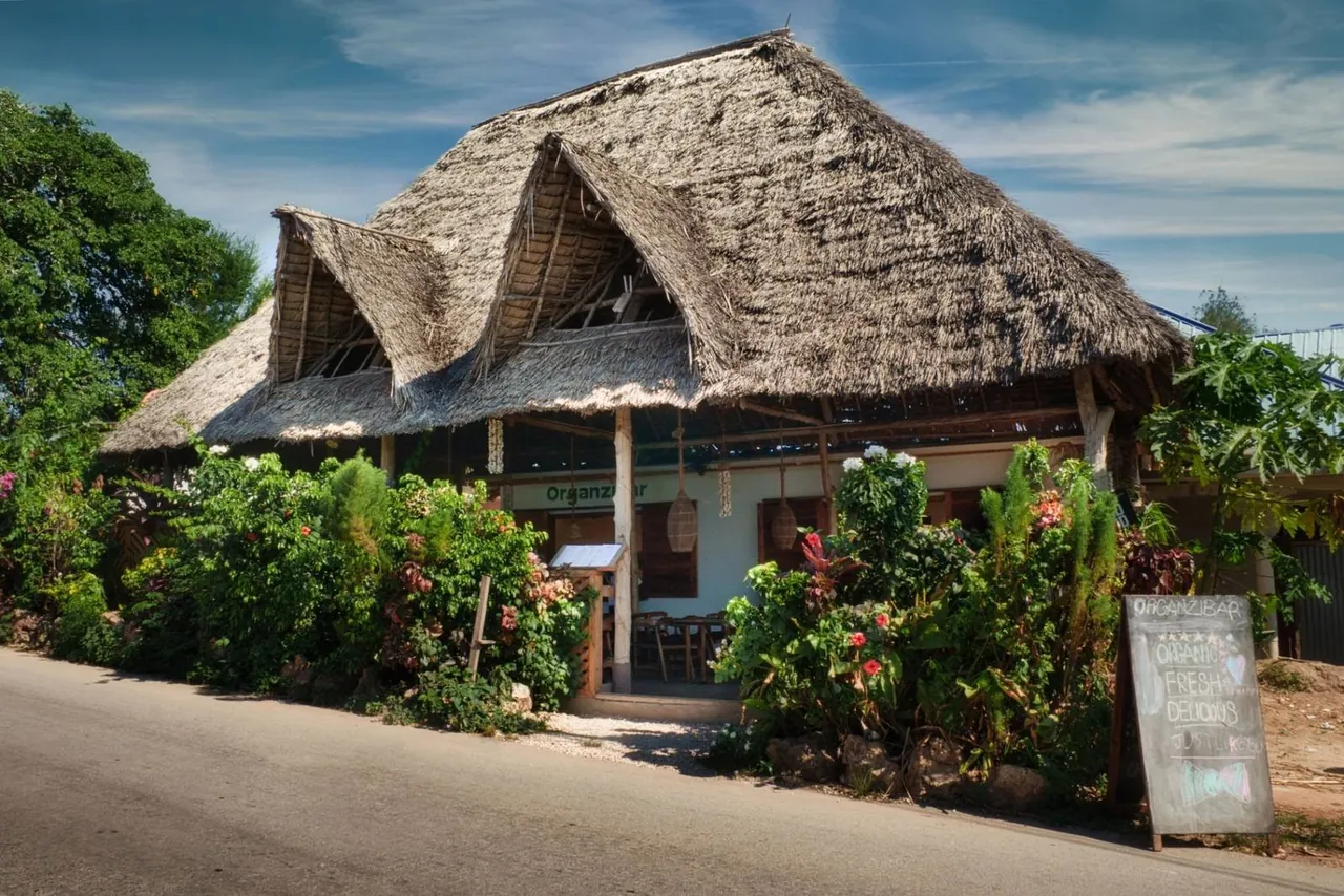 Organzibar's thatched building behind tropical planting beside the road, with a menu board out front
