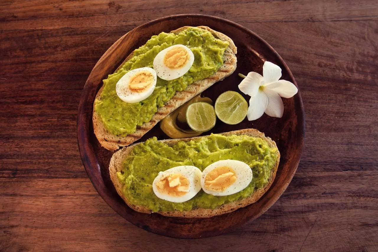 Two slices of avocado toast with boiled eggs and lime on a wooden plate