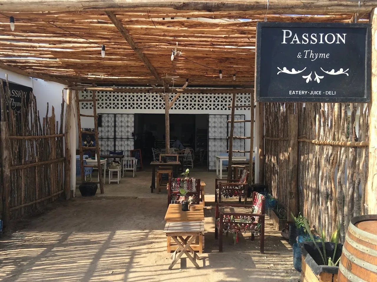 The café's entrance under a stick-thatched pergola, with a Passion & Thyme Eatery Juice Deli sign and tables on sand