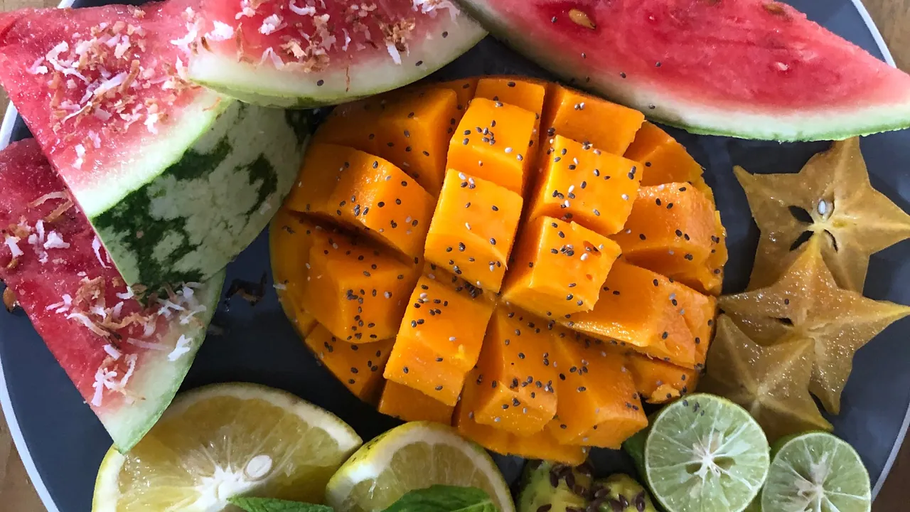 A platter of cut mango, watermelon, star fruit and limes topped with coconut and seeds