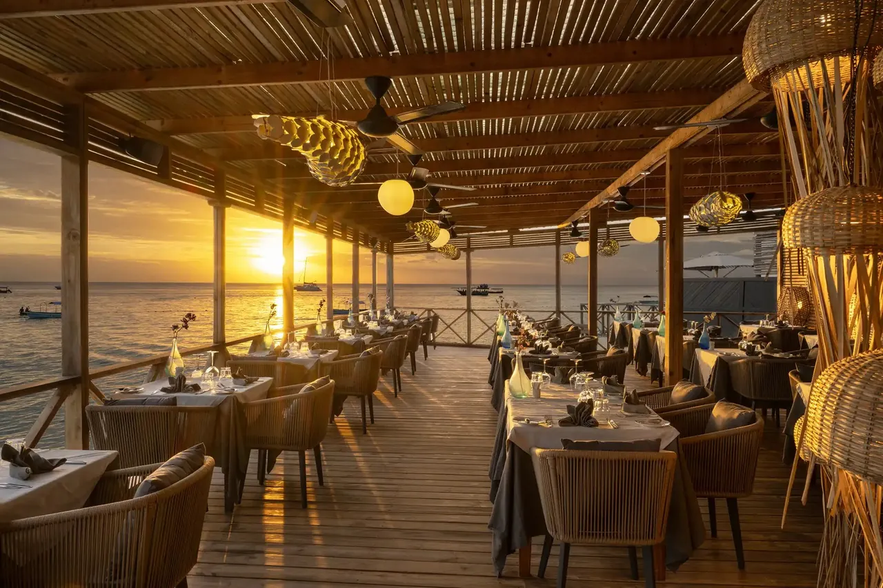 Laid tables on a covered wooden deck looking west over the sea as the sun sets