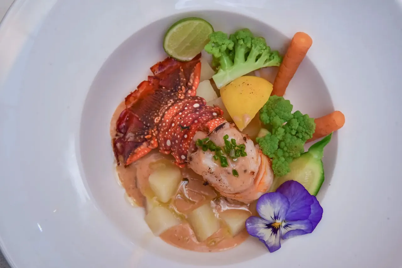 A bowl of lobster and prawn with vegetables, lime and an edible pansy
