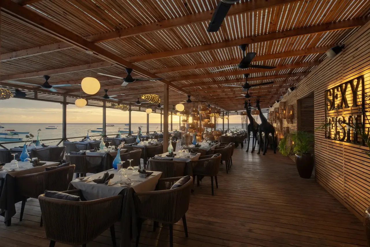 The long covered dining deck with white-clothed tables, wicker chairs and an illuminated Sexy Fish sign