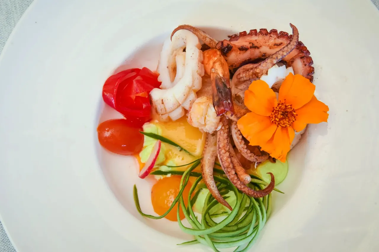 A white plate of grilled octopus, squid and prawns with flowers and spiralised cucumber