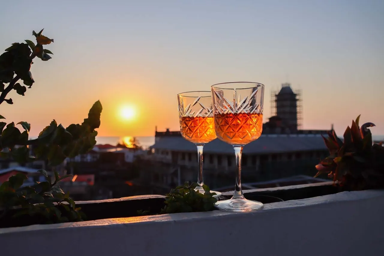 Two cocktails on a parapet with the sun setting behind Stone Town's rooftops and a tower