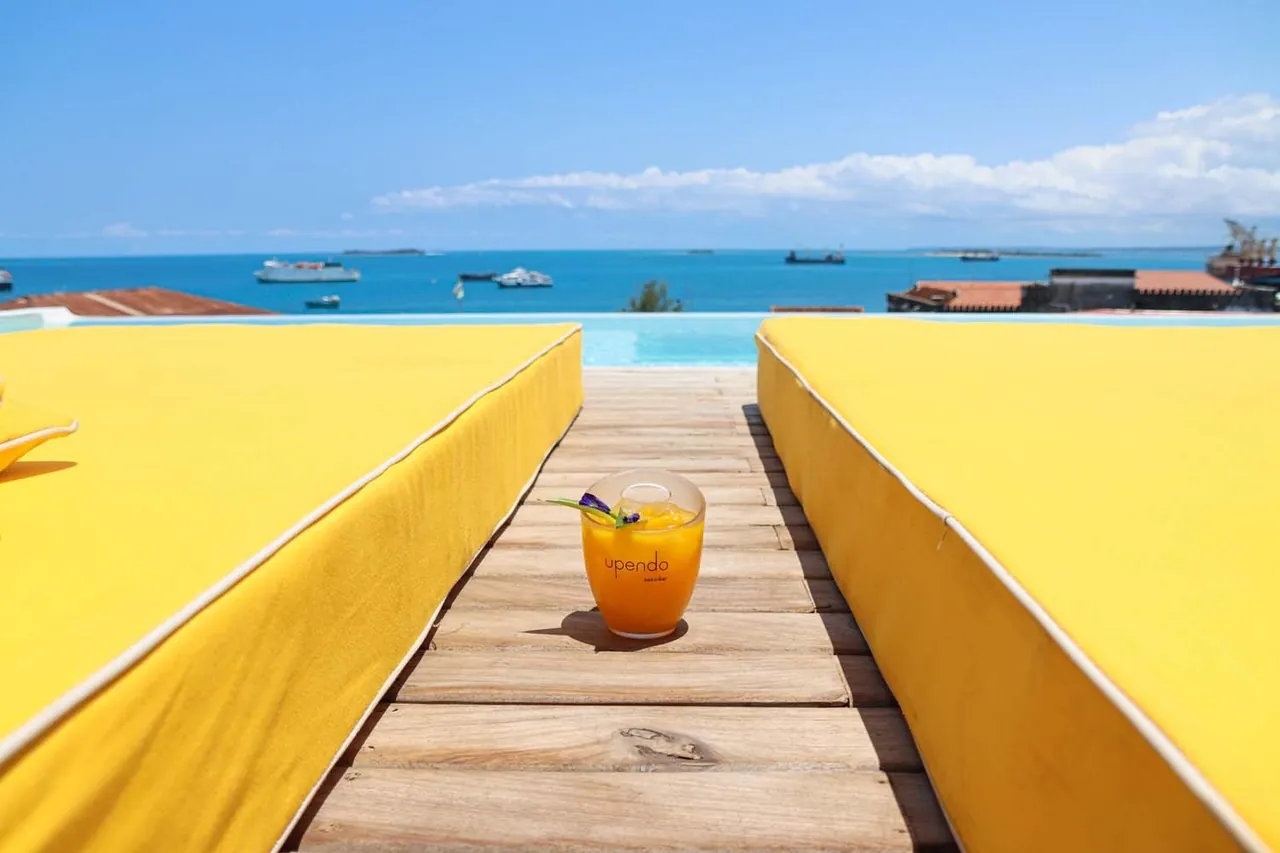 A cocktail on a wooden walkway between yellow loungers, the harbour and ships beyond