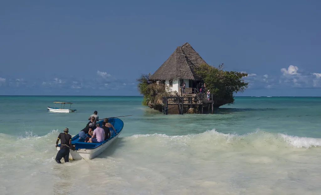 A small blue boat in the surf near the shore carrying guests, with the Rock restaurant behind it.