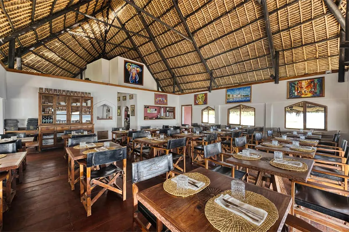 The restaurant's dining room under a high thatched (makuti) roof, with wooden tables and director's chairs.
